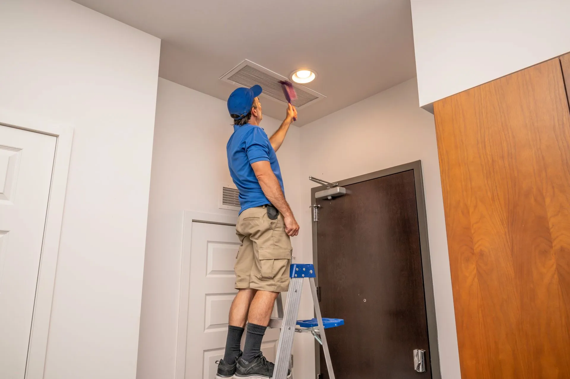 Professional cleaning an air vent while standing on a ladder